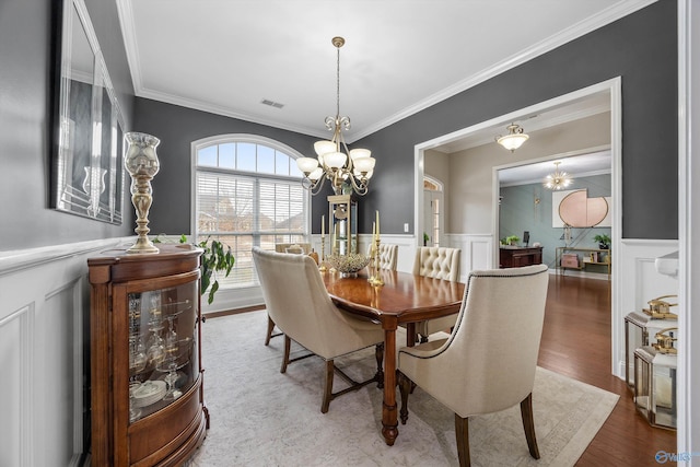 dining room with wood finished floors, visible vents, ornamental molding, wainscoting, and a chandelier