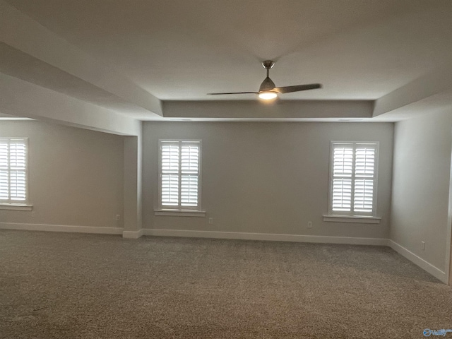 carpeted spare room with a raised ceiling, ceiling fan, and a healthy amount of sunlight