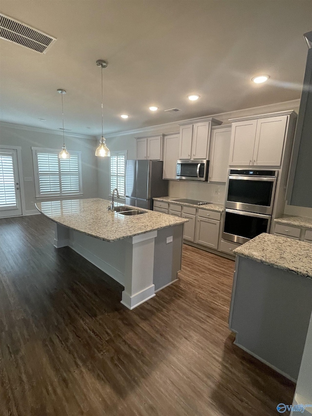 kitchen with decorative light fixtures, sink, stainless steel appliances, and an island with sink