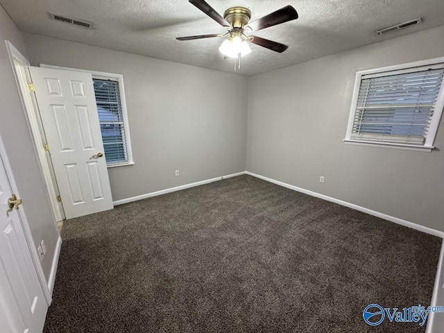 unfurnished bedroom with a textured ceiling, baseboards, visible vents, and dark carpet