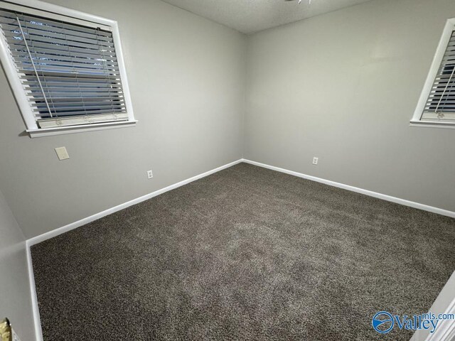 spare room with baseboards and dark colored carpet