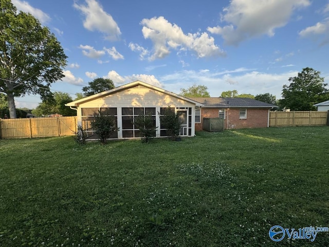 rear view of property featuring a sunroom, brick siding, a lawn, and a fenced backyard