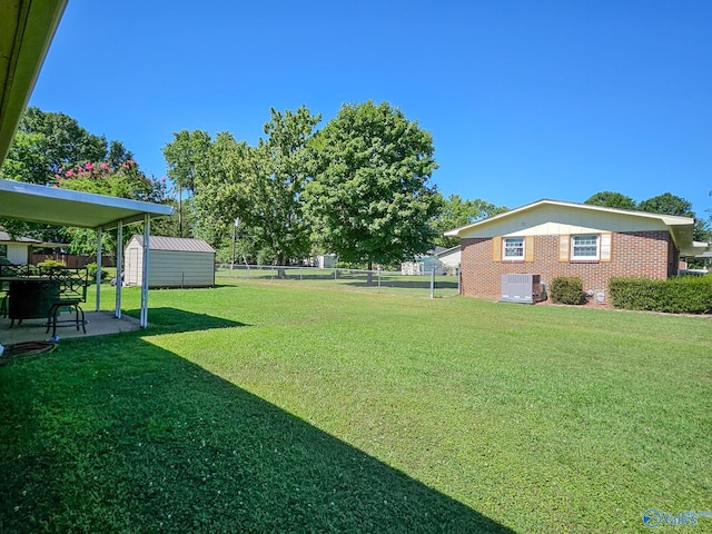 view of yard with an outbuilding, a patio, central AC, fence, and a storage shed