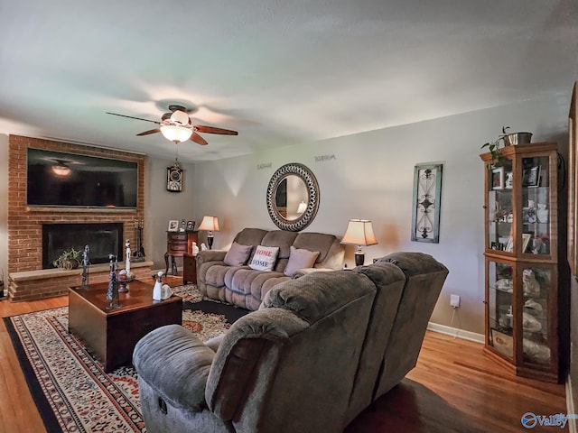 living area featuring a brick fireplace, baseboards, ceiling fan, and wood finished floors