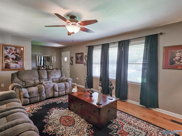 living room with light wood-type flooring, visible vents, baseboards, and a ceiling fan