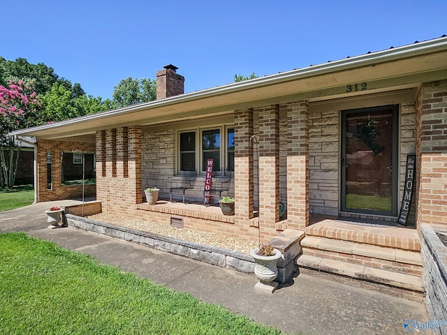 doorway to property featuring brick siding, covered porch, and a chimney