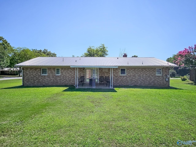 back of house featuring a chimney, metal roof, a yard, and brick siding