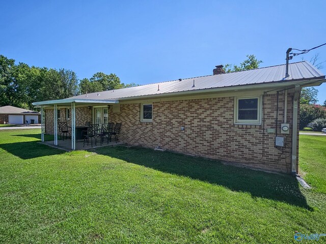 rear view of property with brick siding, a lawn, a chimney, metal roof, and a patio area