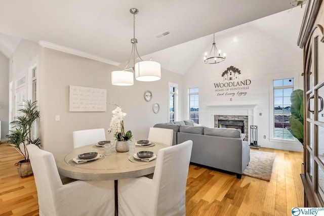 dining area with vaulted ceiling, a stone fireplace, crown molding, and light wood-type flooring