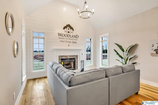 living room with an inviting chandelier, a fireplace, light hardwood / wood-style floors, and vaulted ceiling