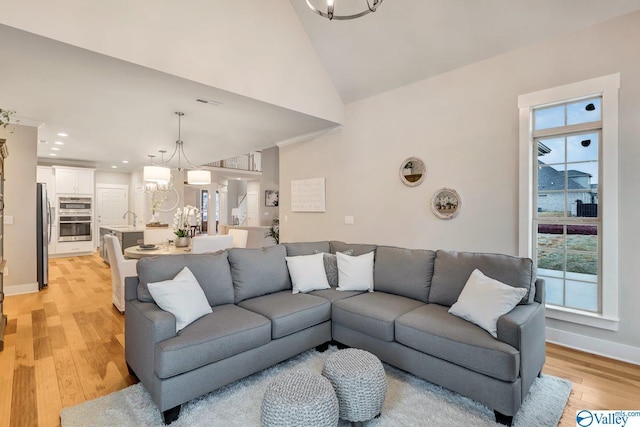 living room featuring a notable chandelier, high vaulted ceiling, sink, and light wood-type flooring