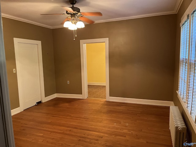spare room featuring baseboards, radiator heating unit, wood finished floors, and crown molding