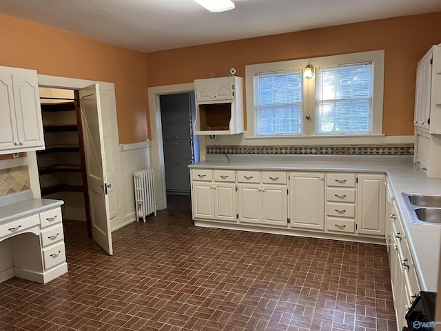 kitchen with radiator, light countertops, backsplash, brick patterned floor, and white cabinets