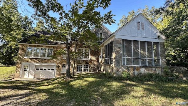 rear view of property featuring stone siding, a yard, an attached garage, and a sunroom