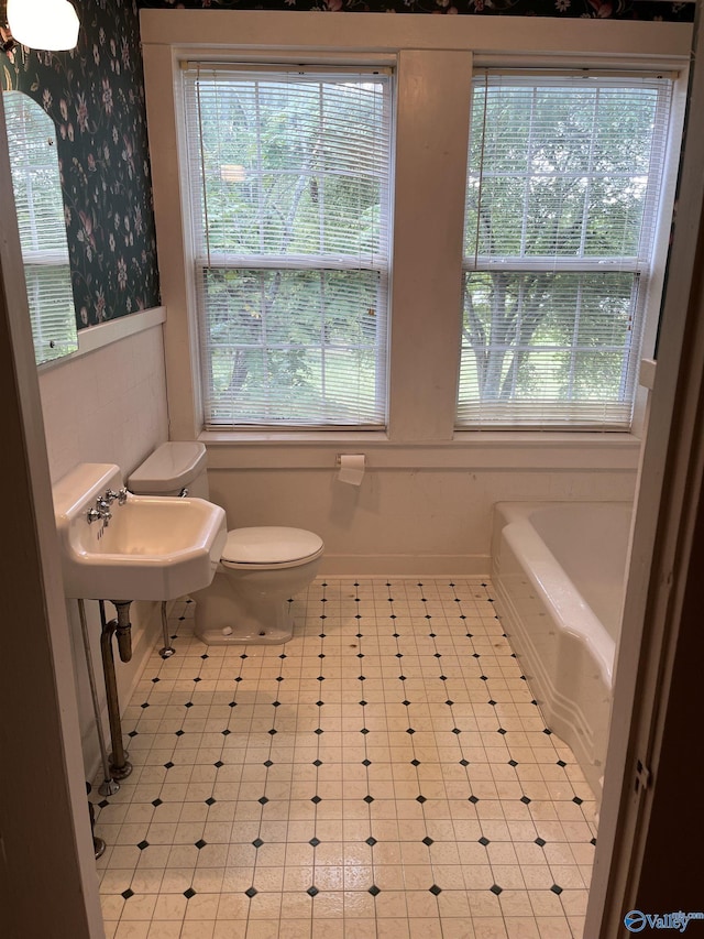 full bathroom with toilet, wallpapered walls, a wealth of natural light, and a wainscoted wall