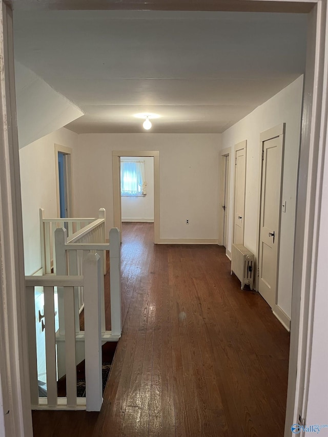corridor featuring radiator, baseboards, dark wood finished floors, and an upstairs landing