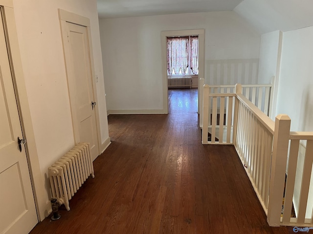 corridor with lofted ceiling, wood finished floors, an upstairs landing, and radiator