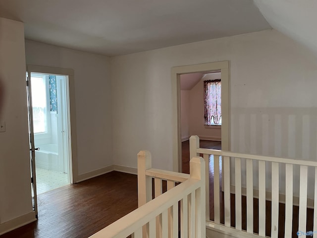 corridor featuring vaulted ceiling, dark wood-type flooring, an upstairs landing, and baseboards