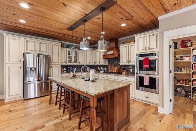 kitchen with light wood-style flooring, stainless steel appliances, tasteful backsplash, a sink, and custom range hood