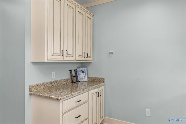 kitchen featuring baseboards, cream cabinets, and light stone counters