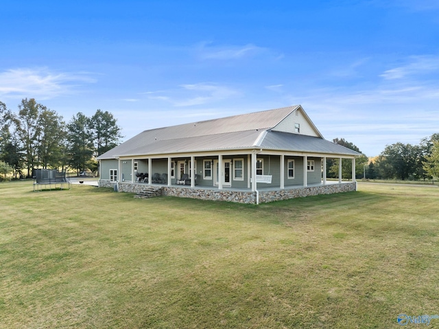 rear view of property featuring metal roof, a trampoline, a porch, and a yard
