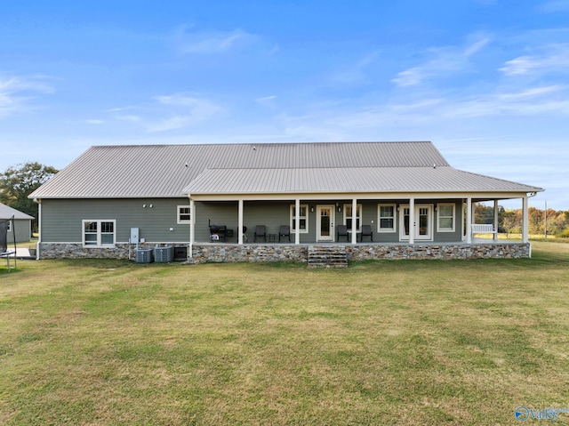 rear view of property featuring cooling unit, metal roof, a trampoline, covered porch, and a lawn