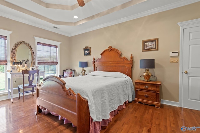 bedroom with baseboards, crown molding, visible vents, a raised ceiling, and wood finished floors