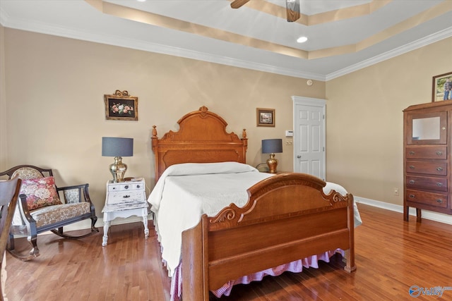 bedroom featuring a tray ceiling, crown molding, wood finished floors, and baseboards