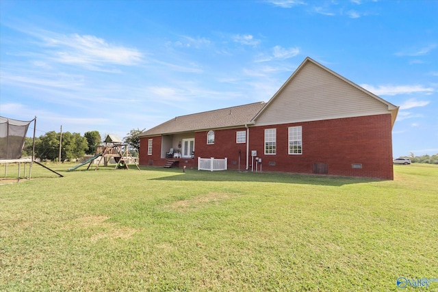 rear view of house featuring a trampoline, a playground, and a lawn