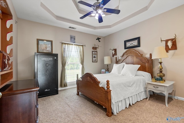 bedroom with a raised ceiling, light colored carpet, and ceiling fan