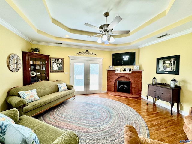 living room with hardwood / wood-style flooring, a fireplace, a raised ceiling, ceiling fan, and ornamental molding