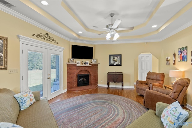 living room with a tray ceiling, wood finished floors, a fireplace, and visible vents