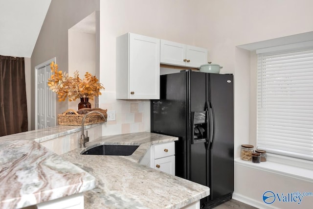 kitchen featuring a sink, backsplash, white cabinets, and black fridge