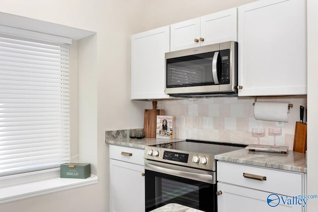 kitchen featuring stainless steel appliances, light stone counters, decorative backsplash, and white cabinets