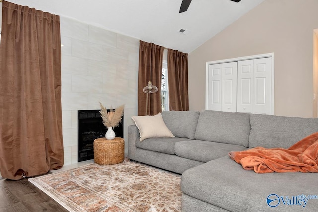 living area featuring lofted ceiling, ceiling fan, a fireplace, wood finished floors, and visible vents