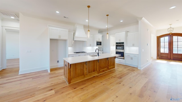 kitchen featuring light wood-style floors, double oven, a sink, stovetop, and premium range hood