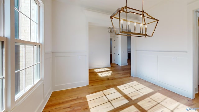 unfurnished dining area with a notable chandelier, light wood-style flooring, a decorative wall, and plenty of natural light