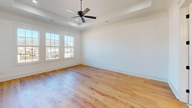 spare room with baseboards, light wood-style flooring, and a tray ceiling
