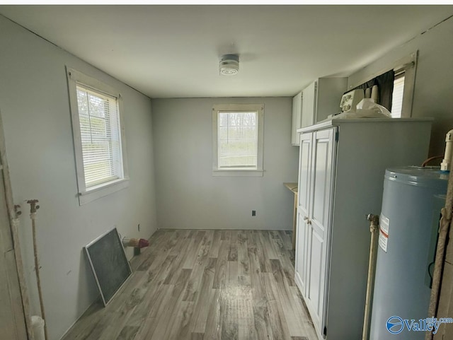 clothes washing area featuring water heater, a healthy amount of sunlight, and light hardwood / wood-style flooring