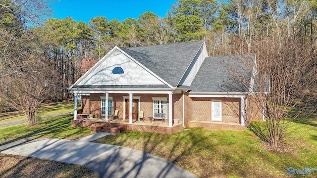 neoclassical home with a front yard, brick siding, covered porch, and roof with shingles