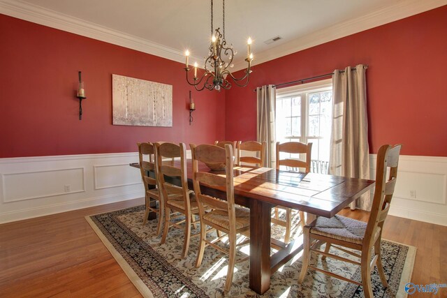 dining area featuring light wood-type flooring, visible vents, an inviting chandelier, crown molding, and wainscoting