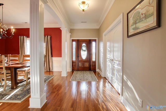 foyer entrance with wood finished floors, visible vents, ornate columns, an inviting chandelier, and crown molding