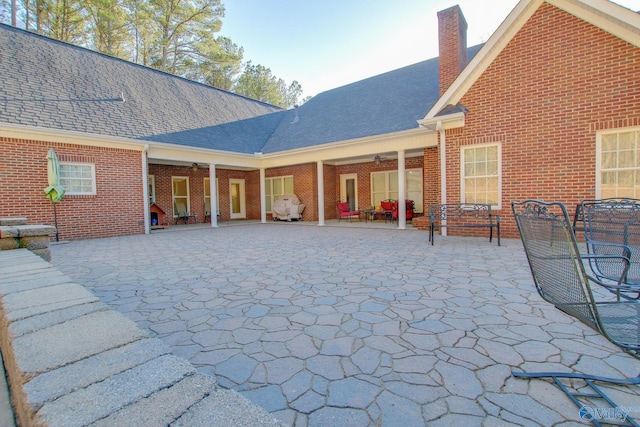 back of house featuring brick siding, a chimney, a patio, and roof with shingles