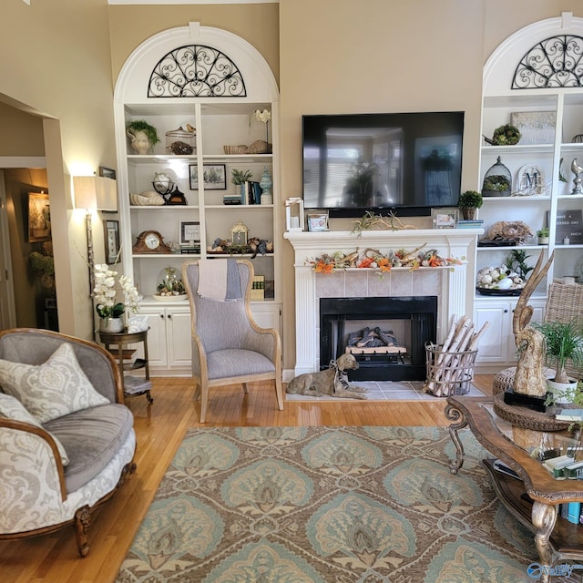 living area with a towering ceiling, a tiled fireplace, and light wood-type flooring