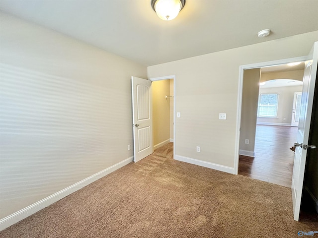 unfurnished bedroom featuring baseboards, arched walkways, and carpet flooring