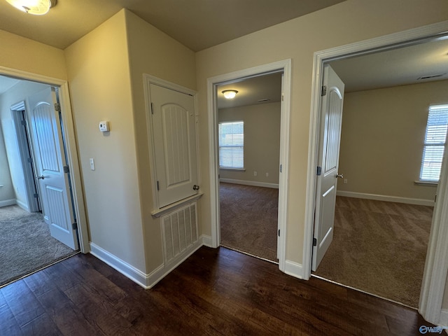 hall featuring dark wood finished floors, visible vents, dark carpet, and baseboards