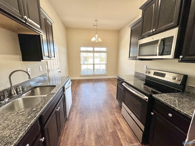 kitchen featuring dark stone counters, dark wood-style flooring, a sink, stainless steel appliances, and pendant lighting