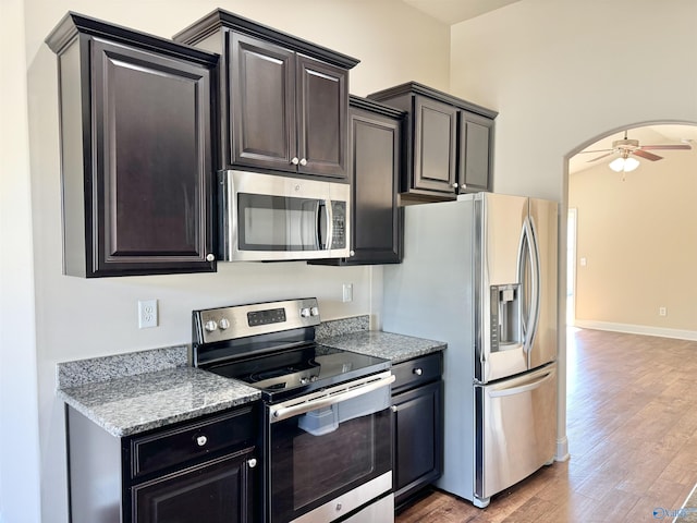 kitchen with light wood-type flooring, arched walkways, appliances with stainless steel finishes, baseboards, and ceiling fan