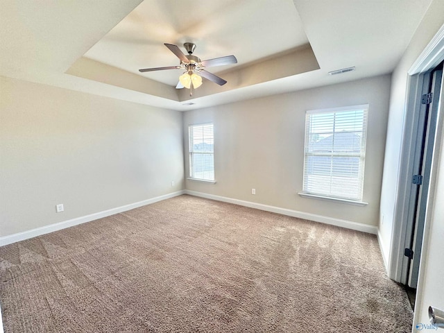 spare room with carpet, baseboards, visible vents, a tray ceiling, and ceiling fan