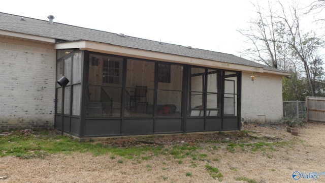 back of house featuring fence, brick siding, a shingled roof, and a sunroom